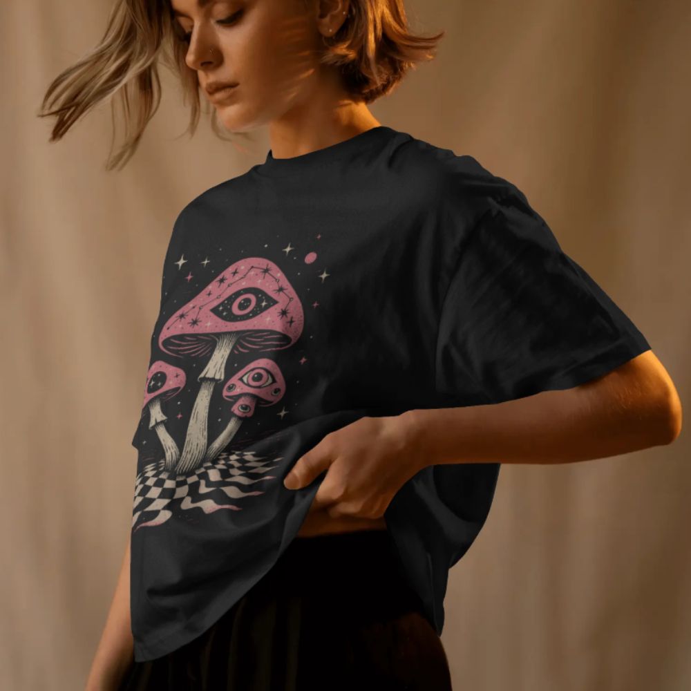 Female model wearing black psychedelic mushroom eye T-shirt with surreal cosmic illustration