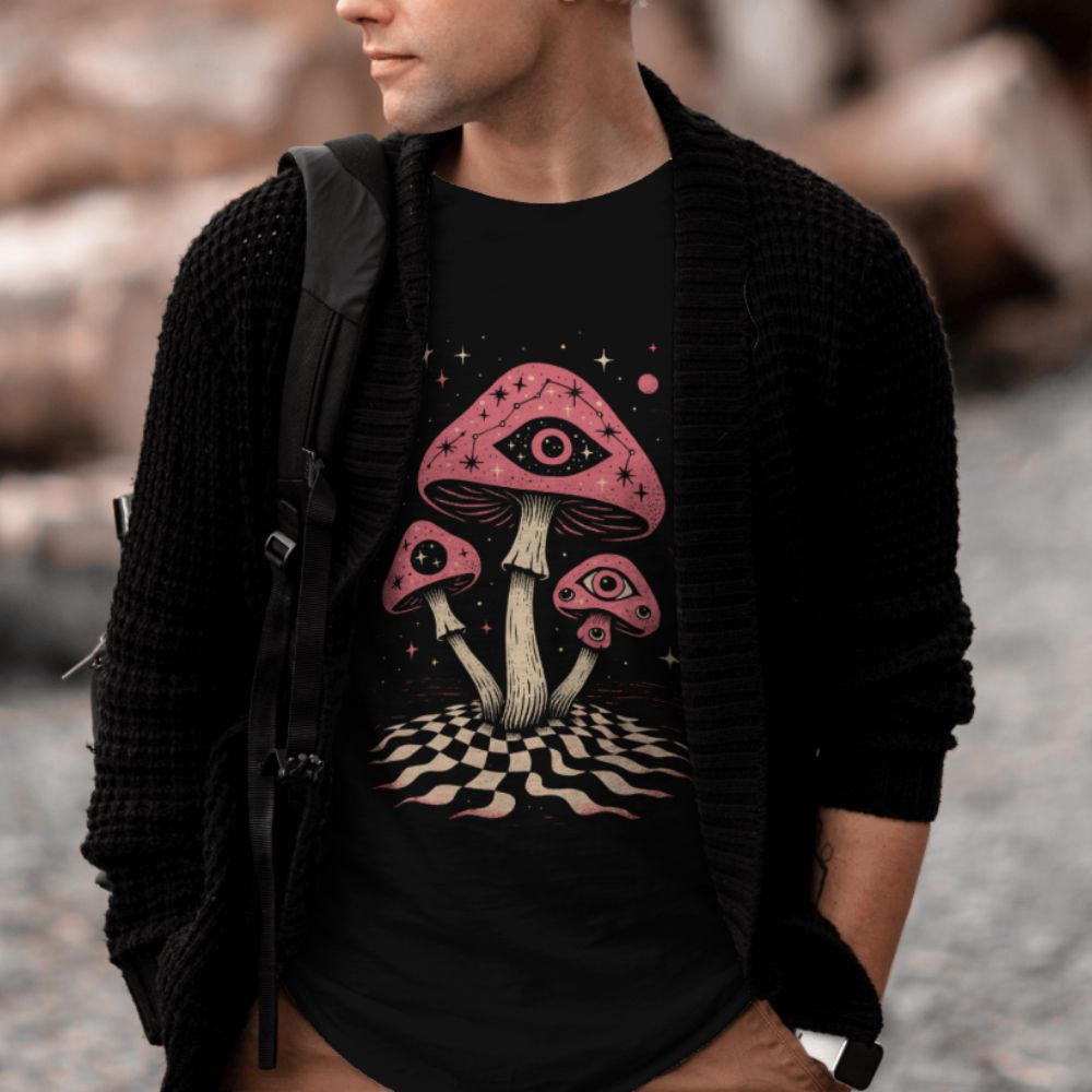 Male model wearing black surreal mushroom eye graphic T-shirt styled in outdoor lifestyle setting