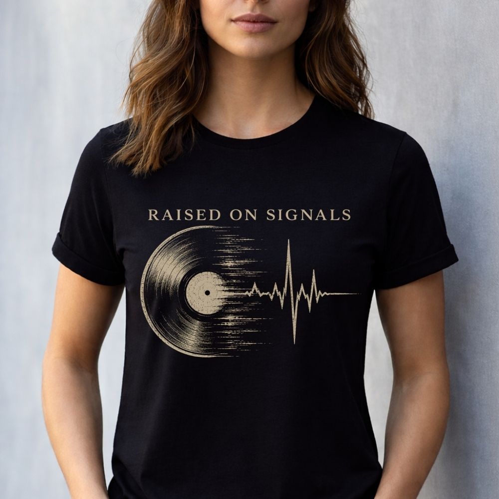 Person wearing a black t-shirt with a vinyl record and heartbeat design, text 'Raised on Signals'.