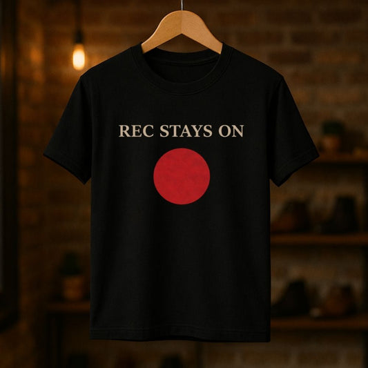 Black t-shirt with red circle and 'REC STAYS ON' text on a wooden hanger against a dark background