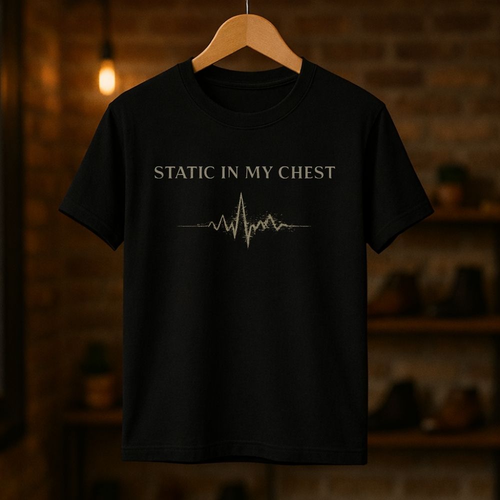 Black t-shirt with 'Static in My Chest' text and heartbeat line on a wooden hanger against a dark background.