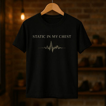 Black t-shirt with 'Static in My Chest' text and heartbeat line on a wooden hanger against a dark background.