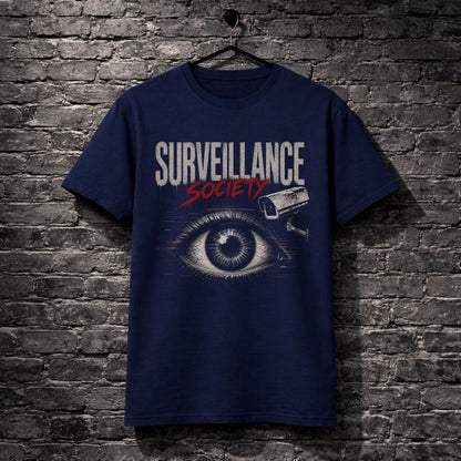 A navy blue graphic t-shirt hanging on a black hanger against a dark gray brick wall. The shirt features a graphic print with the text 'SURVEILLANCE SOCIETY' in white and red, an eye illustration, and a security camera icon.