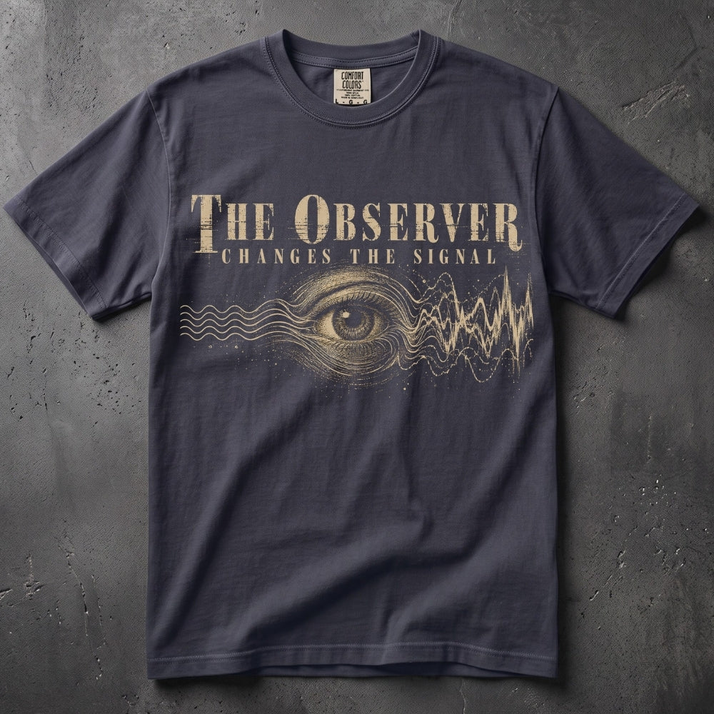 A dark navy blue graphic t-shirt laid flat on a textured gray background. The shirt features a gold-colored print of an eye, sound waves, and the text 'THE OBSERVER CHANGES THE SIGNAL'.