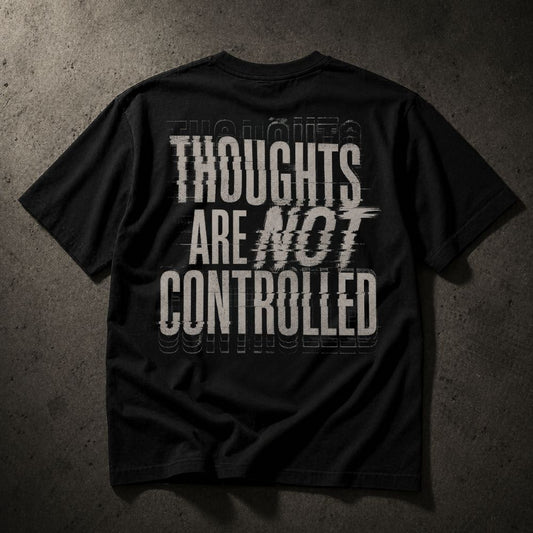 A black short-sleeve t-shirt laid flat against a dark textured gray background, featuring a distressed white graphic text print on the back that reads 'THOUGHTS ARE NOT CONTROLLED'.