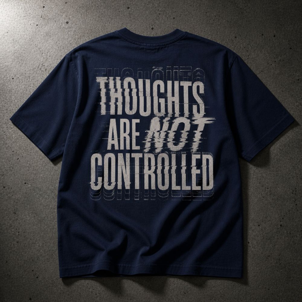 A navy blue t-shirt with a large white graphic text print reading 'THOUGHTS ARE NOT CONTROLLED' on the back, laid flat on a textured gray concrete surface.