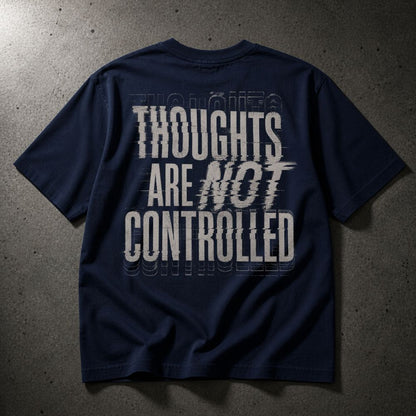 A navy blue t-shirt with a large white graphic text print reading 'THOUGHTS ARE NOT CONTROLLED' on the back, laid flat on a textured gray concrete surface.