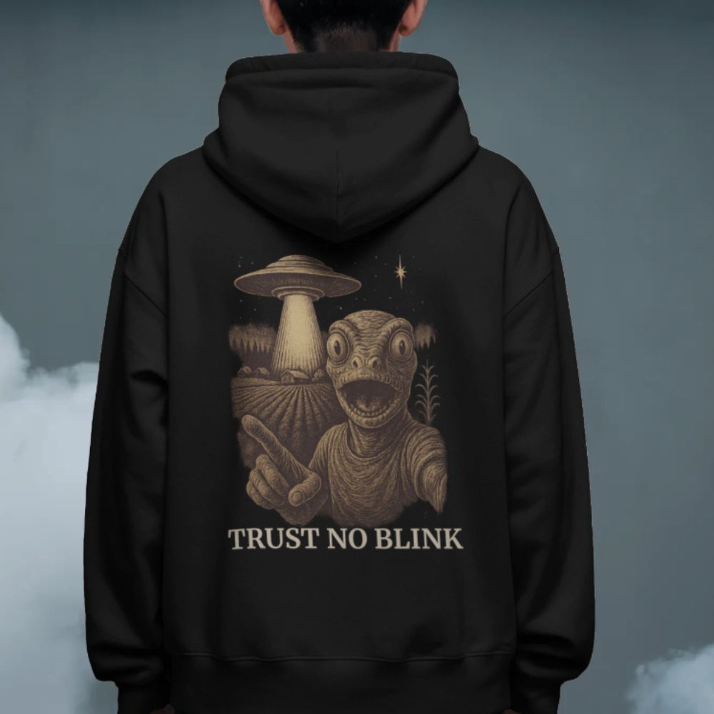 Person wearing a black hoodie with a “Trust No Blink” alien and UFO sci-fi artwork printed on the back.