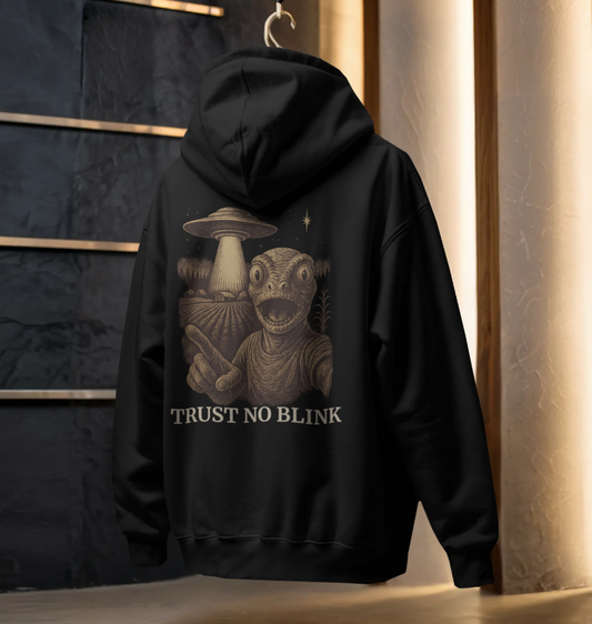 Black hoodie with “Trust No Blink” back print featuring an alien figure pointing toward a UFO in a surreal sci-fi illustration.