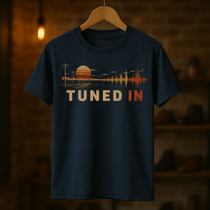 Navy blue t-shirt with 'Tuned In' graphic design on a wooden hanger against a dark background