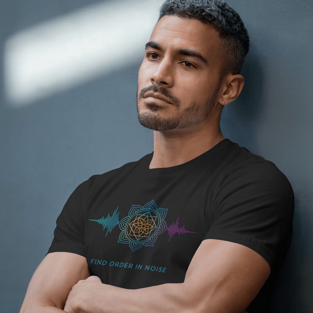 Man wearing black “Find Order in Noise” T-shirt with colorful mandala and waveform design, leaning against gray wall.