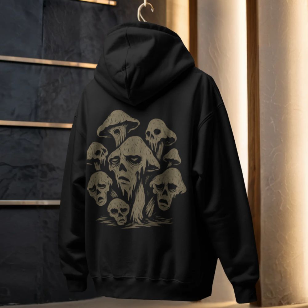 Black hoodie with surreal mushroom skull illustration printed on the back, hanging in a modern studio setting.