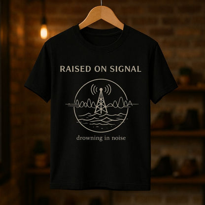 Black t-shirt with 'Raised on Signal' design on a wooden hanger against a dark background