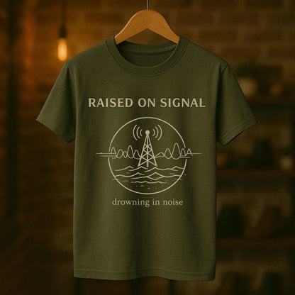 Green t-shirt with 'Raised on Signal' design on a wooden hanger against a blurred background