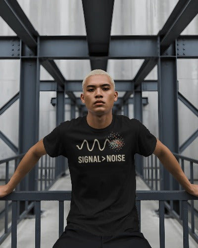 Man wearing Twistbug black t-shirt with ‘Signal > Noise’ design, sitting confidently on an industrial steel bridge