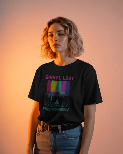 Woman wearing Twistbug black t-shirt with neon glitch graphic reading ‘Signal Lost Find Yourself,’ standing in warm orange studio light.