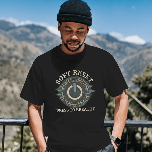 Man wearing black “Soft Reset” T-shirt featuring digital power button design, standing outdoors with mountains in background.