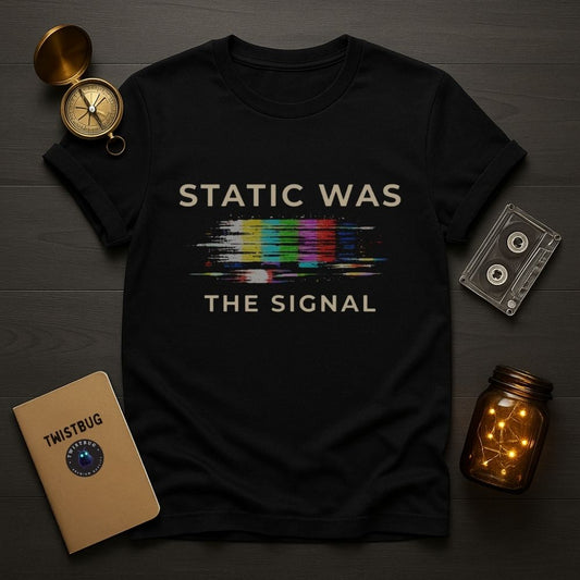 Black t-shirt with 'STATIC WAS THE SIGNAL' text and rainbow design, surrounded by vintage items on a wooden surface.