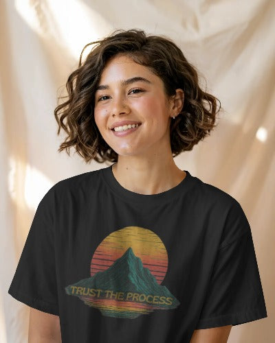 Woman wearing black Twistbug “Trust the Process” T-shirt with retro mountain and sunset design, smiling in natural light.