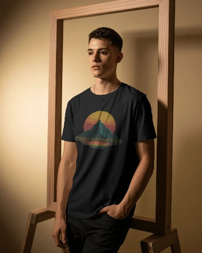 Man wearing navy Twistbug “Trust the Process” T-shirt with mountain graphic and warm retro tones, posing in wooden frame studio.