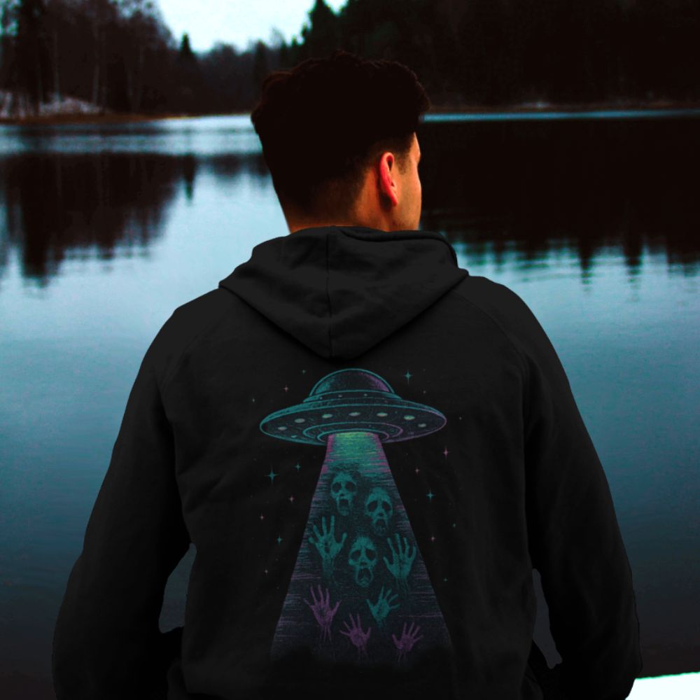 Black hoodie worn from behind outdoors, featuring a surreal UFO abduction design with skulls and reaching hands in a cosmic beam.