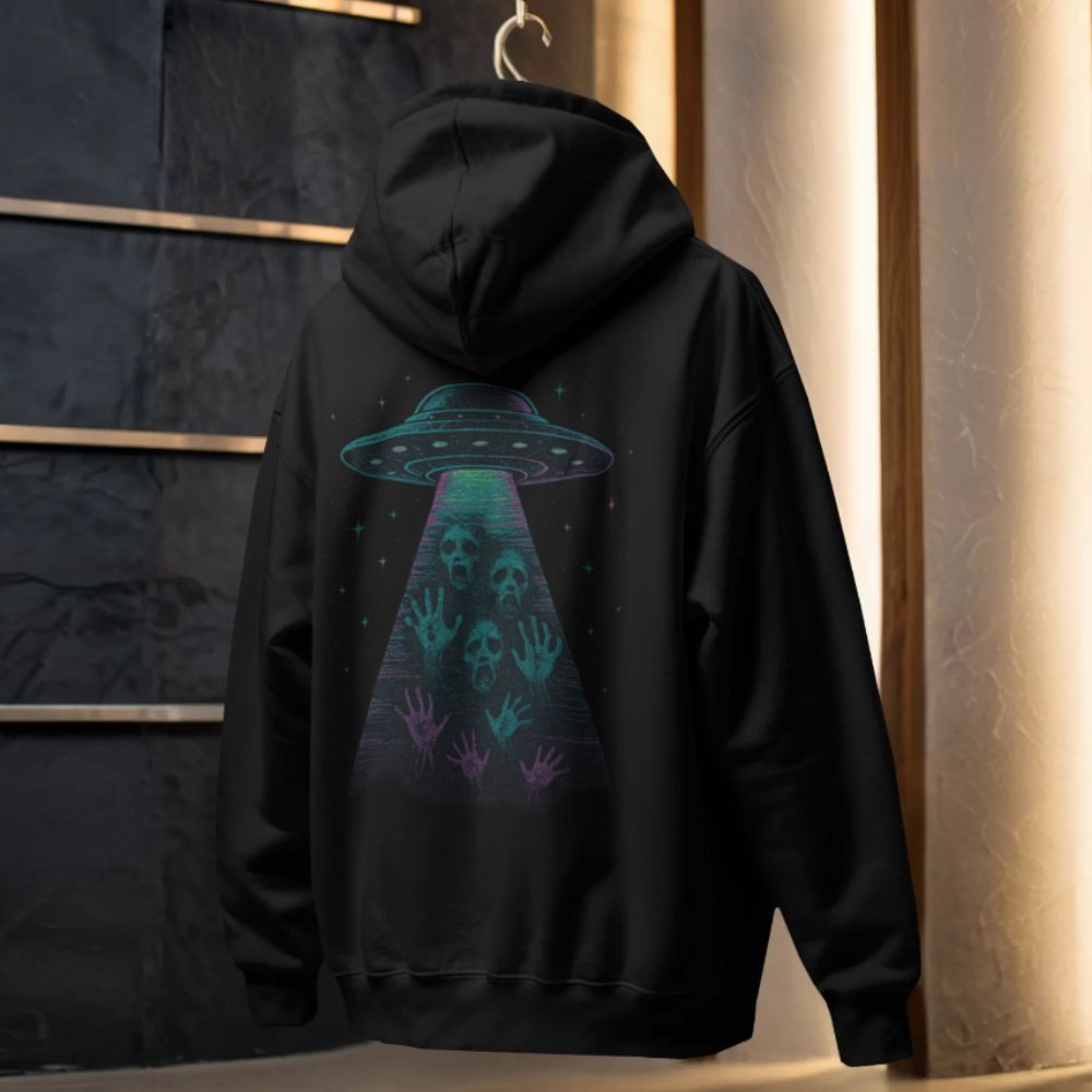 Black hoodie hanging in studio, back view showing a glowing UFO abduction graphic with skulls and hands in a cosmic beam.