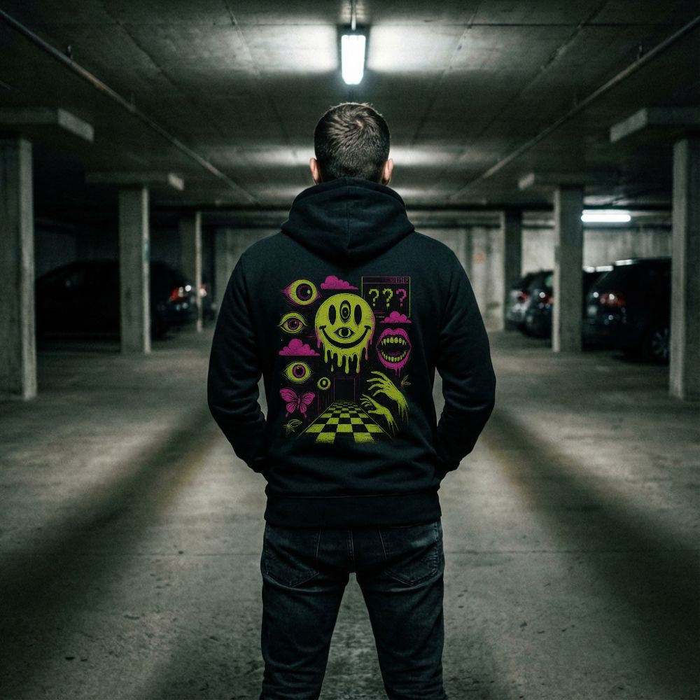 Back view of a black hoodie with neon surreal smiley and eye graphics worn in a dim parking garage