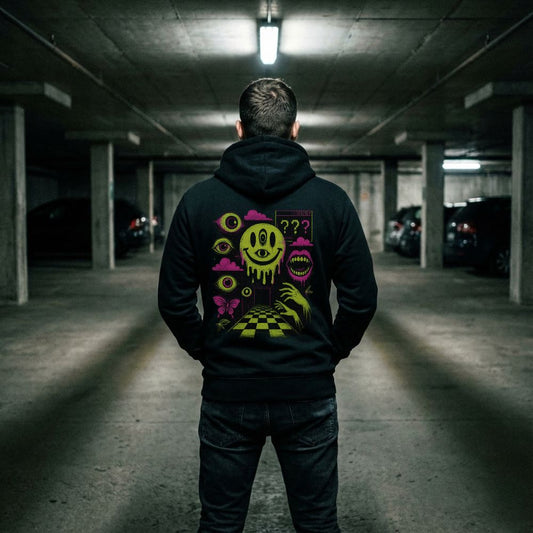Back view of a black hoodie with neon surreal smiley and eye graphics worn in a dim parking garage