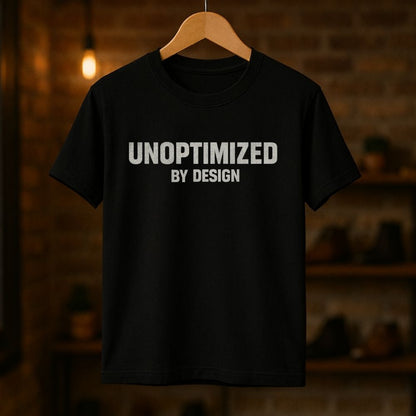 Black t-shirt with 'UNOPTIMIZED BY DESIGN' text on a wooden hanger against a dark background.