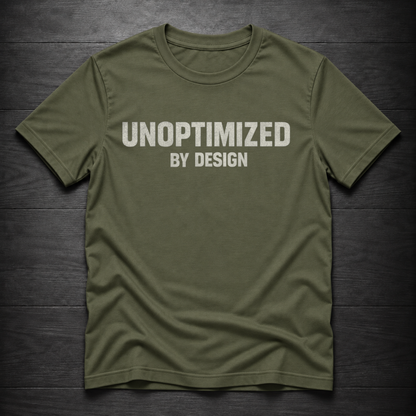An olive green crewneck t-shirt with the text 'UNOPTIMIZED BY DESIGN' printed in white across the chest, laid flat on a dark wood plank background.