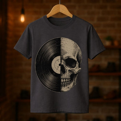 A dark charcoal gray t-shirt hanging on a wooden hanger against a warm, blurred brick wall background. The t-shirt features a graphic print of a vinyl record and a human skull split down the middle.