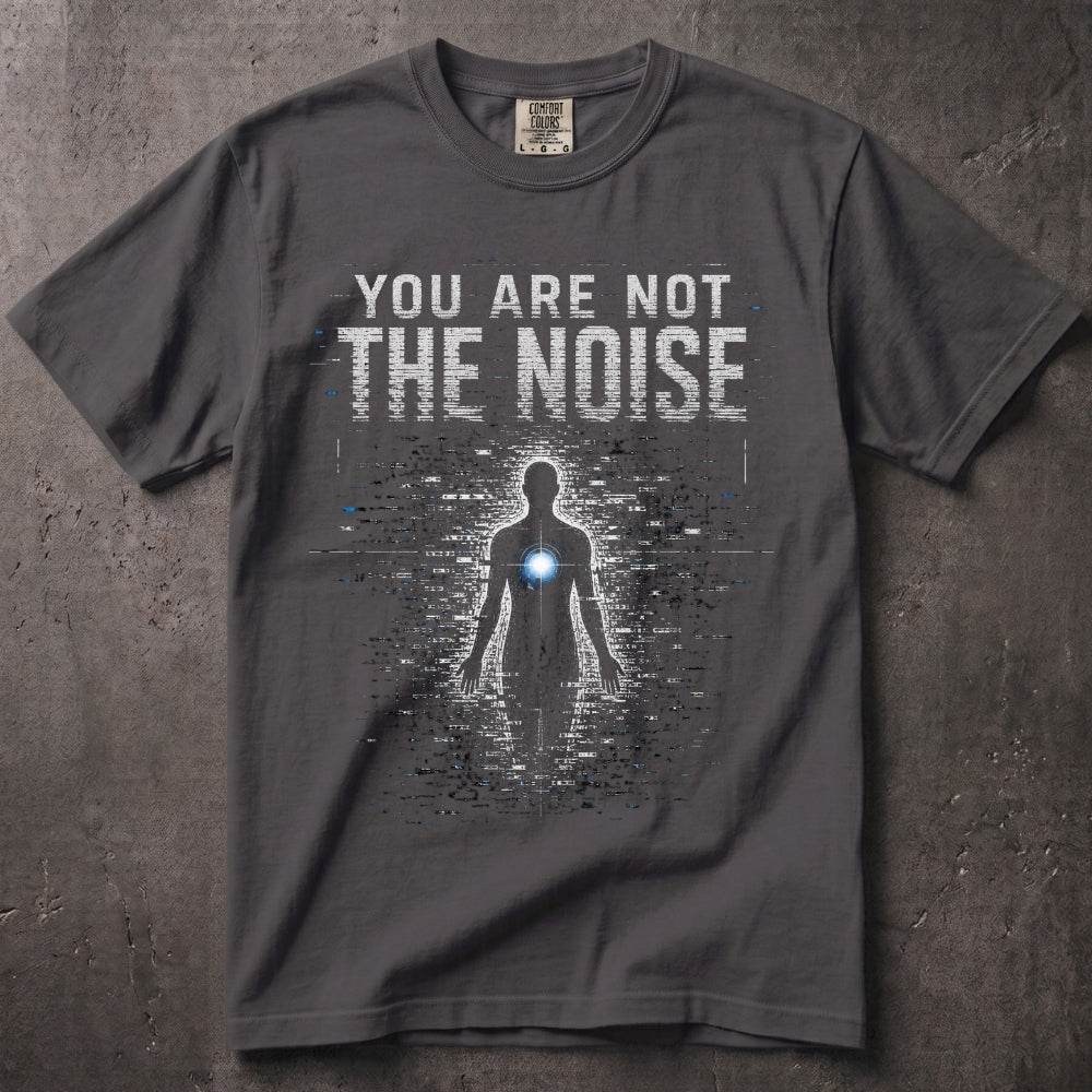 A dark gray graphic t-shirt laid flat on a textured gray background. The shirt features a white and gray digital glitch design with a glowing blue light on the chest and the text 'YOU ARE NOT THE NOISE'.